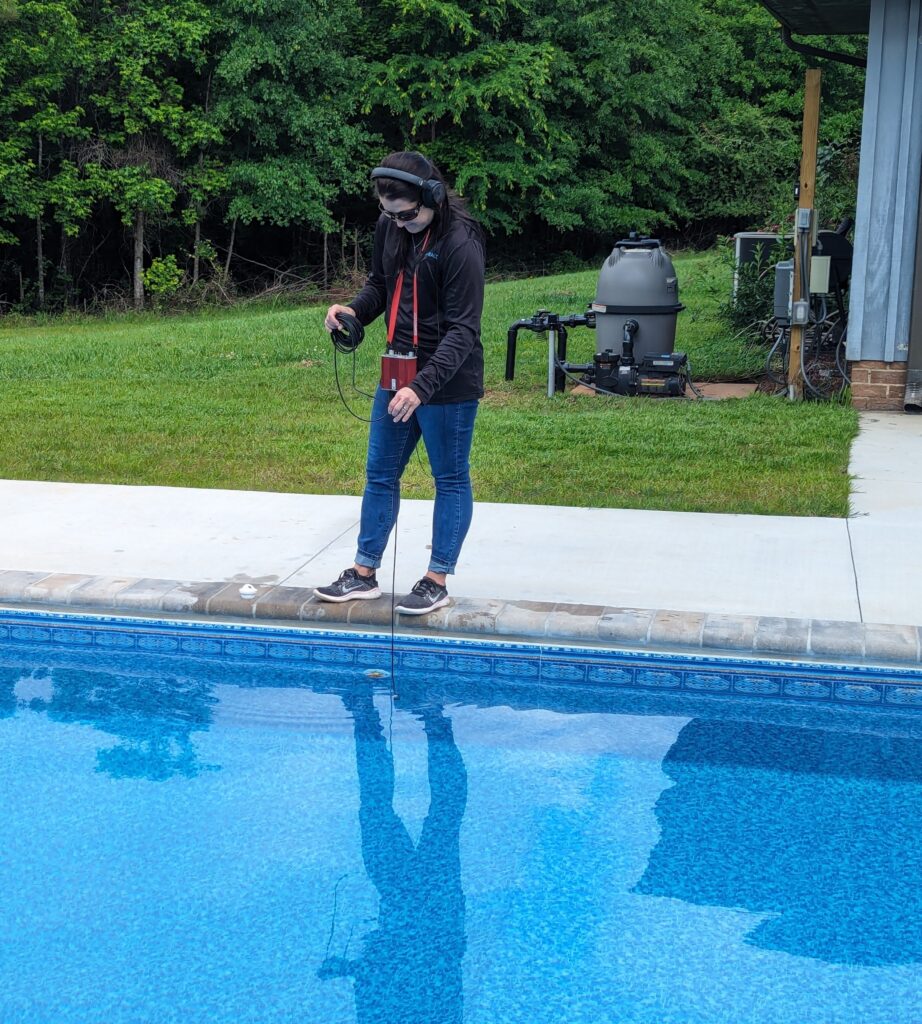 A professional leak detection technician walking beside an above-ground pool using electronic listening equipment to locate hidden leaks.