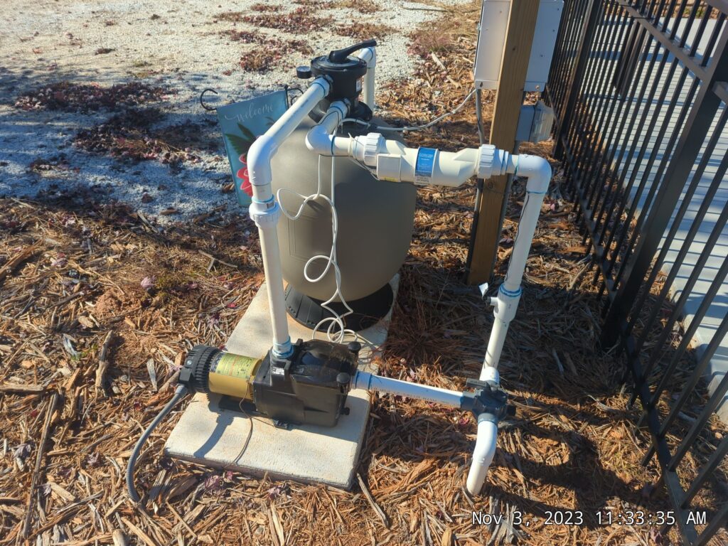 A swimming pool pump and filtration system installed outdoors next to a fenced pool area.