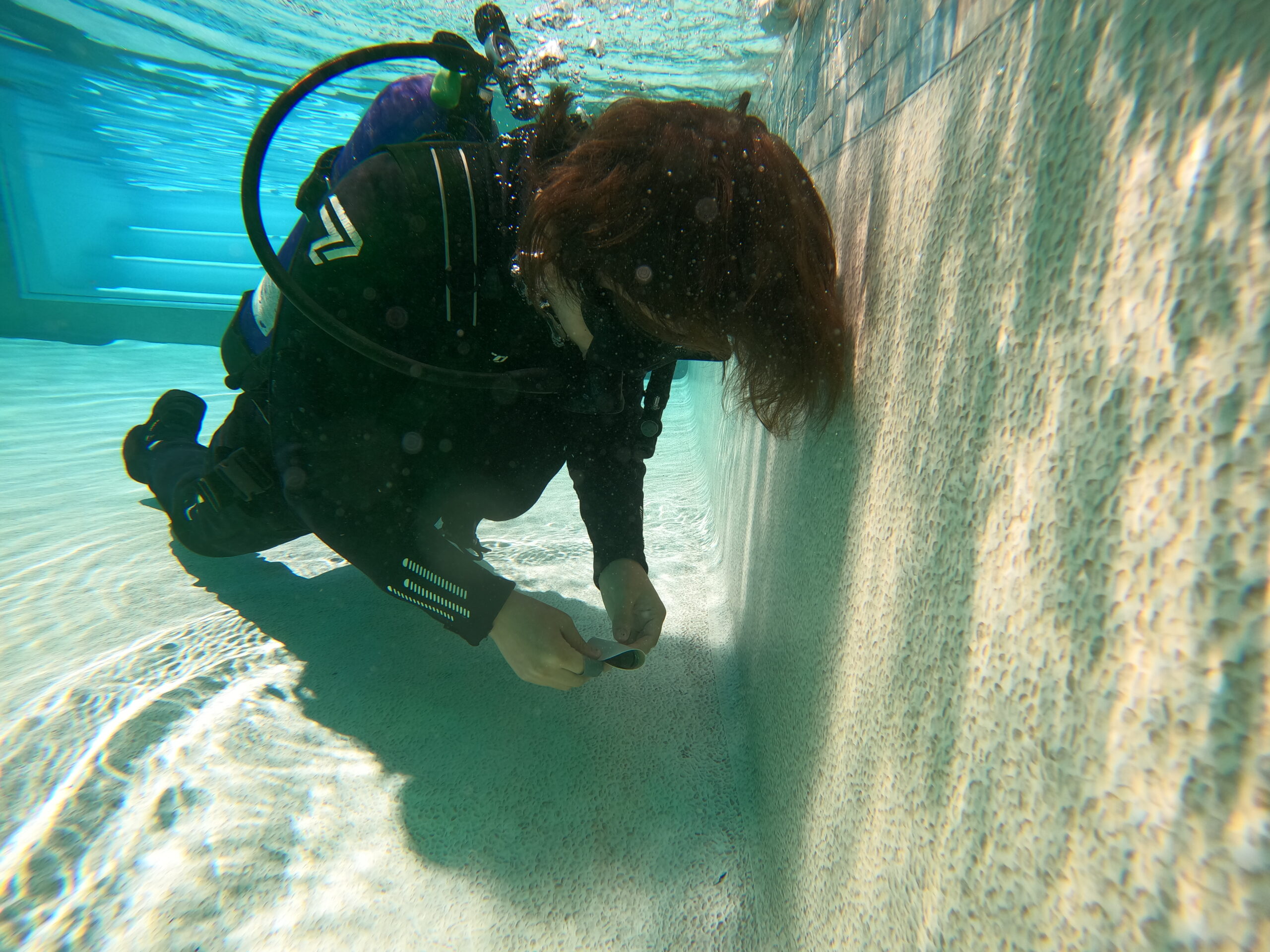 Pool leak detection technician performing visual survey in SCUBA gear at a residential pool equipment pad — professional leak detection in progress