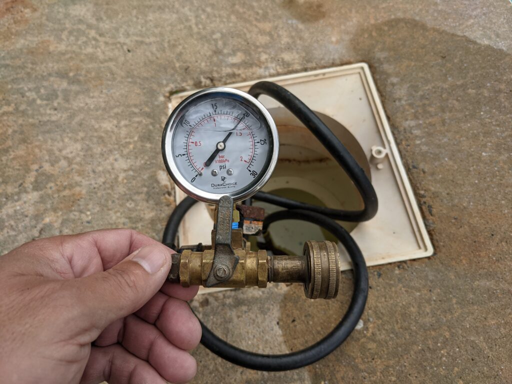 Pressure gauge connected to pool plumbing during a leak detection pressure test — monitoring for pressure loss that confirms an underground leak